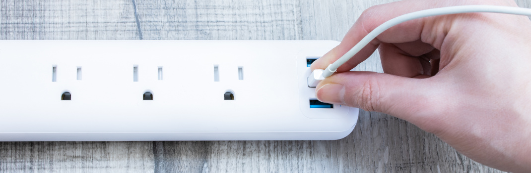 A hand plugging a cord into the USB port on a surge protector