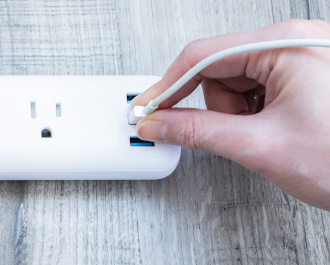 A hand plugging a cord into the USB port on a surge protector