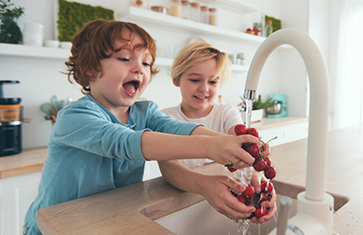 Two children rinsing cherries in the kitchen sink