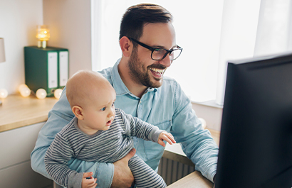 A father holding his baby while smiling at a computer screen