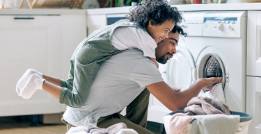 A father does the laundry with his laughing child on his back