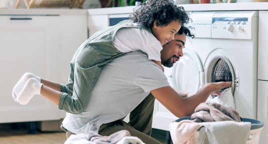 A father does the laundry with his laughing child on his back