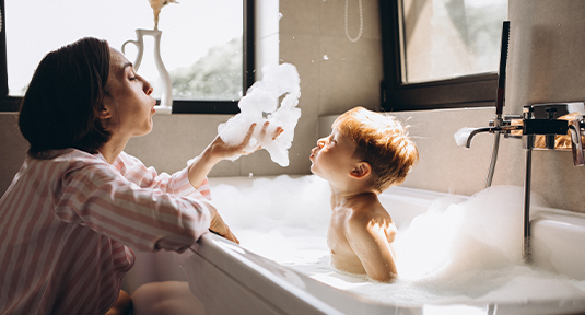A mother giving baby son a bubble bath and blowing bubbles
