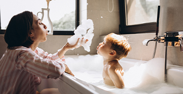 A mother giving baby son a bubble bath and blowing bubbles